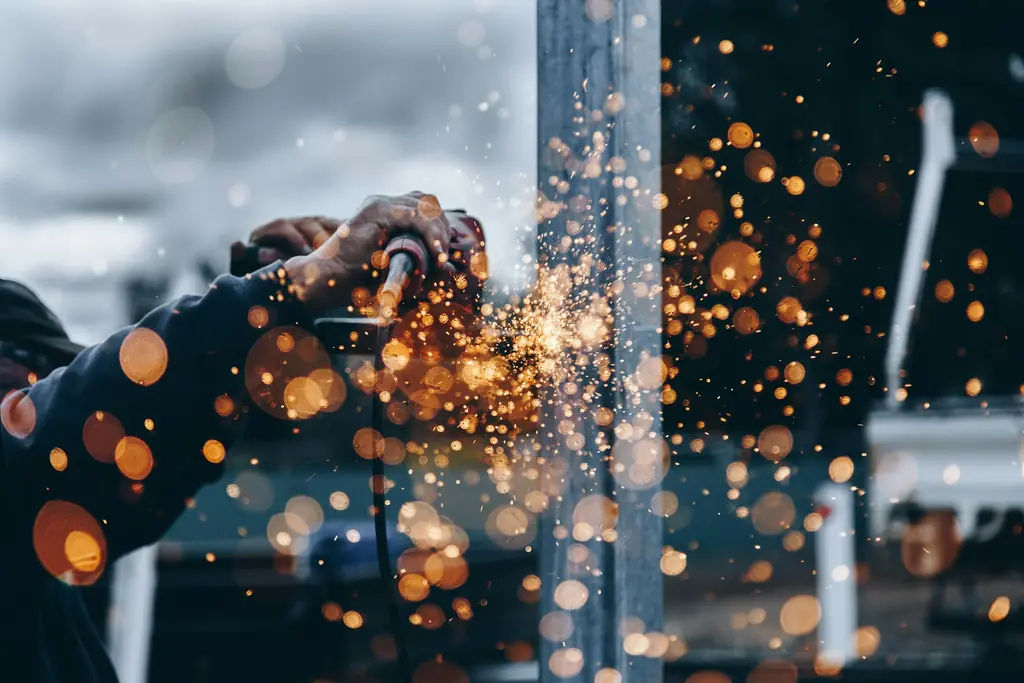Technicien en atelier sur une pièce métallique, gerbe d'étincelles